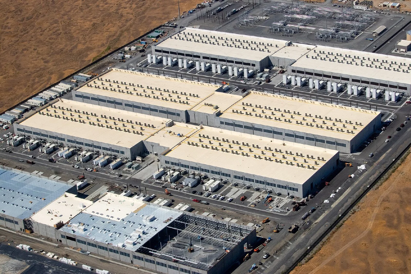 Several large, windowless AWS data center buildings in a flat rural landscape, with another building under construction